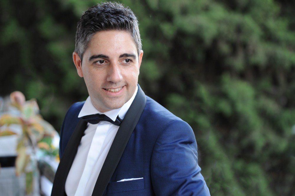 Ο Γιάννης, φορόντας ένα κοστούμι σε μπλε σκούρη απόχρωση, με μαύρες λεπτομέρειες